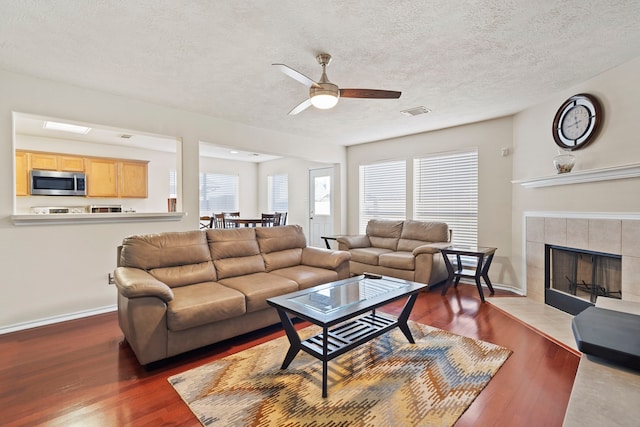 living room with plenty of natural light, dark hardwood / wood-style flooring, a tiled fireplace, and a textured ceiling