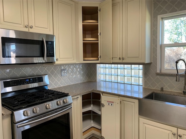 kitchen with sink, light stone counters, tasteful backsplash, appliances with stainless steel finishes, and cream cabinetry