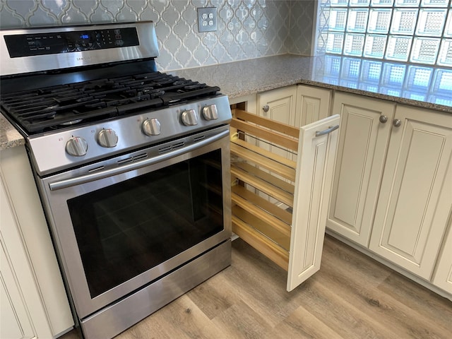 kitchen with light stone counters, stainless steel range with gas stovetop, light hardwood / wood-style floors, and cream cabinetry