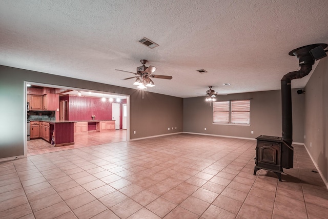 unfurnished living room with light tile patterned flooring, a wood stove, a textured ceiling, and ceiling fan