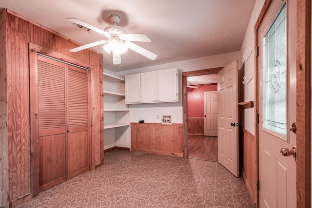 kitchen featuring white cabinetry, ceiling fan, and wood walls