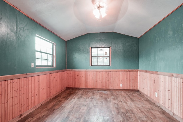 unfurnished room with ceiling fan, wood walls, vaulted ceiling, and light wood-type flooring