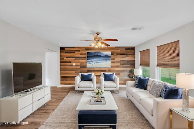 living room featuring light hardwood / wood-style floors, ceiling fan, and wood walls