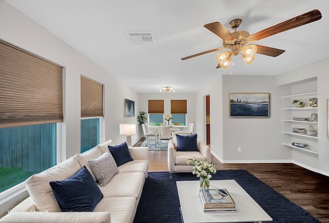 living room featuring dark wood-type flooring, ceiling fan, and built in features