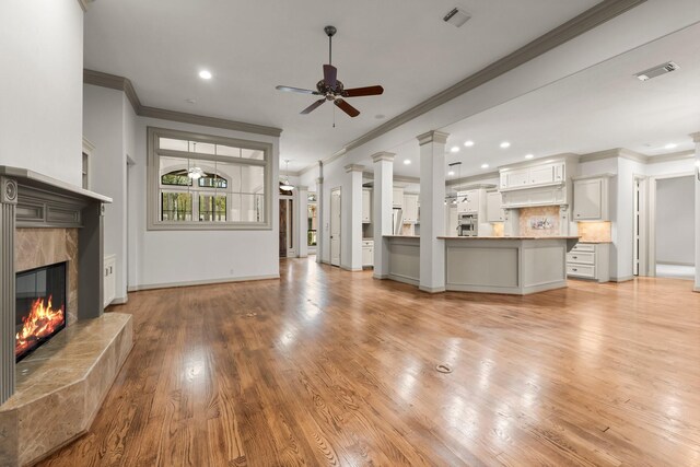 unfurnished living room with crown molding, ceiling fan, decorative columns, a fireplace, and light hardwood / wood-style floors