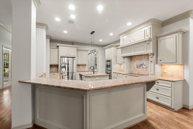 kitchen with appliances with stainless steel finishes, white cabinetry, an island with sink, decorative light fixtures, and kitchen peninsula