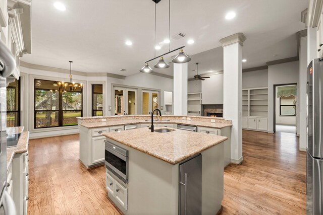 kitchen featuring sink, a kitchen island with sink, hanging light fixtures, stainless steel appliances, and white cabinets