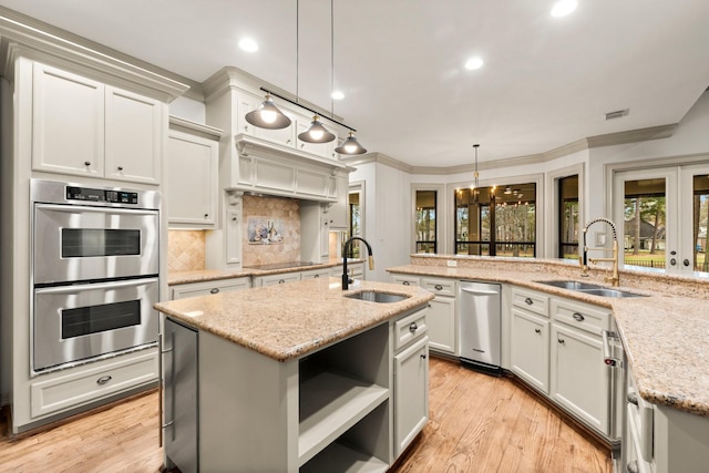 kitchen featuring sink, light stone counters, pendant lighting, stainless steel appliances, and a kitchen island with sink