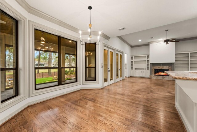 unfurnished living room with built in shelves, wood-type flooring, ornamental molding, and ceiling fan with notable chandelier