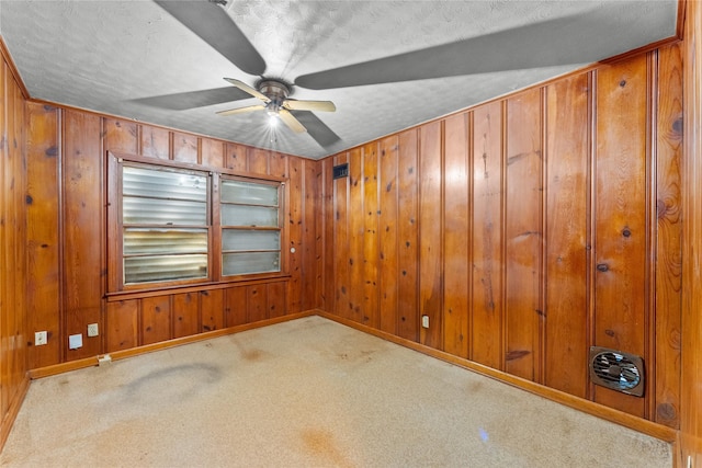 carpeted empty room featuring ceiling fan, a textured ceiling, and wood walls