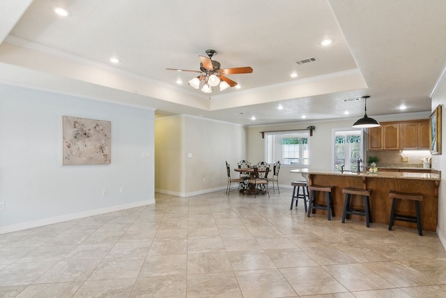 kitchen featuring a raised ceiling, ornamental molding, a breakfast bar area, and light stone counters