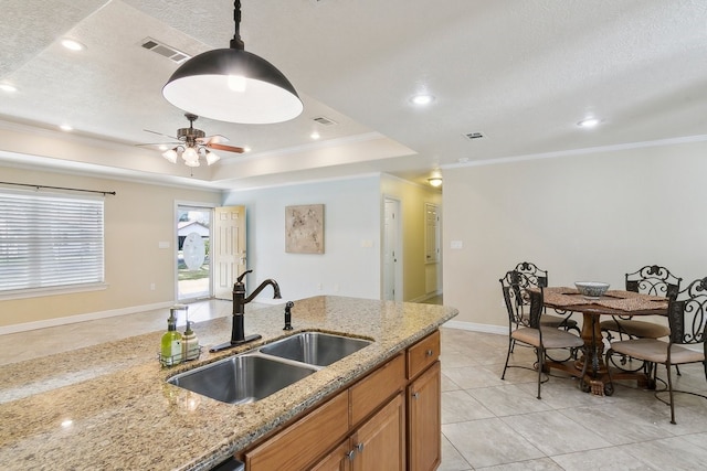 kitchen with sink, light stone counters, hanging light fixtures, ornamental molding, and a tray ceiling