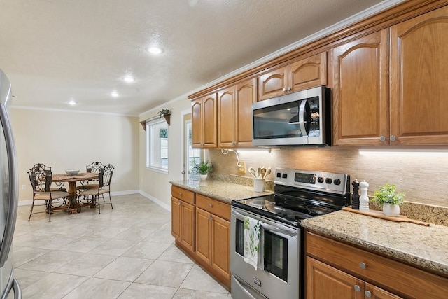 kitchen featuring appliances with stainless steel finishes, backsplash, ornamental molding, light tile patterned floors, and light stone counters