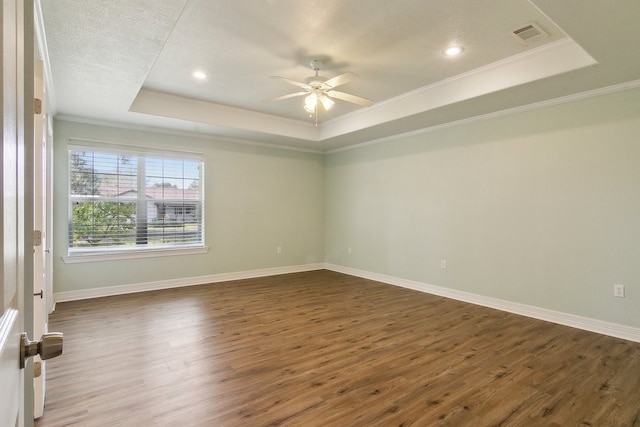 empty room featuring a tray ceiling, dark wood-type flooring, and ornamental molding