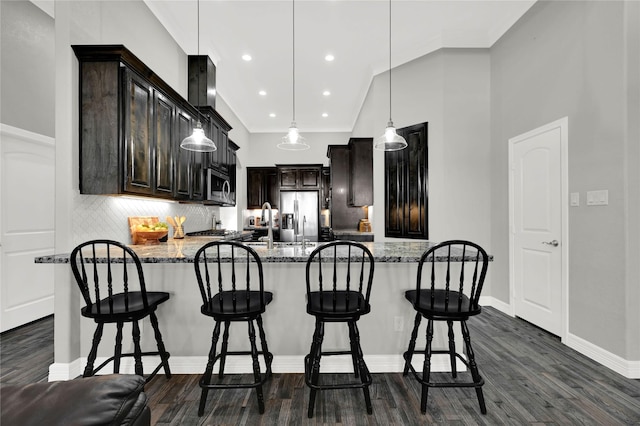 kitchen with stainless steel appliances, a peninsula, dark wood-style floors, and light stone countertops