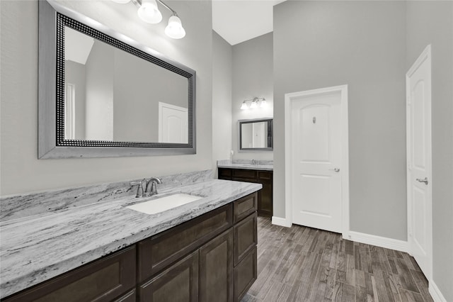 full bath with wood finished floors, two vanities, a sink, and baseboards