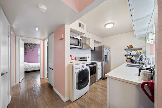 kitchen with stainless steel appliances, washer / dryer, light hardwood / wood-style floors, and white cabinets