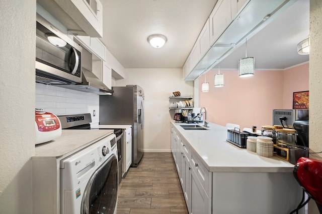 kitchen with sink, hanging light fixtures, appliances with stainless steel finishes, washer / clothes dryer, and white cabinets