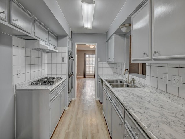 kitchen with gray cabinets, appliances with stainless steel finishes, sink, decorative backsplash, and light wood-type flooring