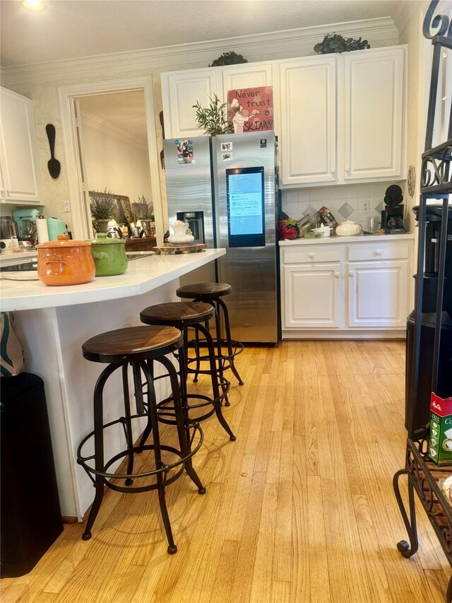 kitchen with a kitchen bar, white cabinetry, stainless steel fridge with ice dispenser, light hardwood / wood-style floors, and decorative backsplash