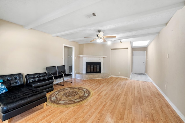 living room featuring ceiling fan, a skylight, beamed ceiling, and light wood-type flooring