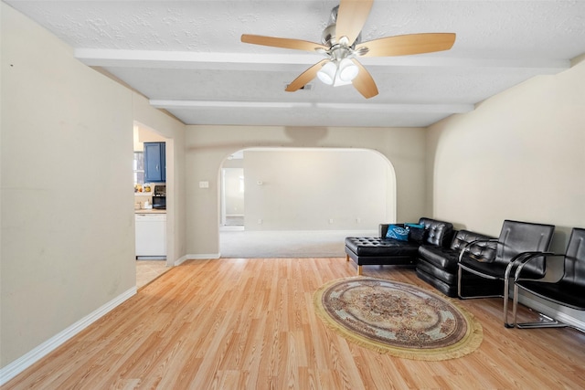 living room with ceiling fan, wood-type flooring, beam ceiling, and a textured ceiling