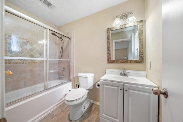 full bathroom featuring vanity, a textured ceiling, enclosed tub / shower combo, and toilet