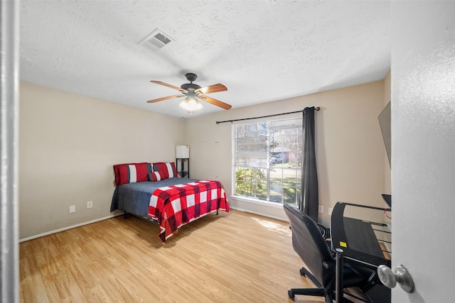 bedroom with a textured ceiling, ceiling fan, and light wood-type flooring