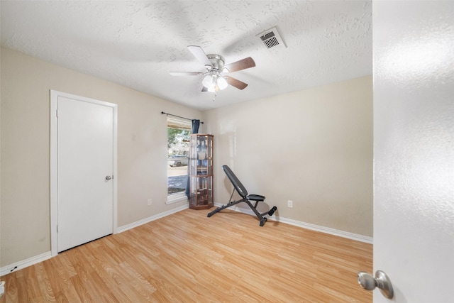 workout area with ceiling fan, a textured ceiling, and light wood-type flooring