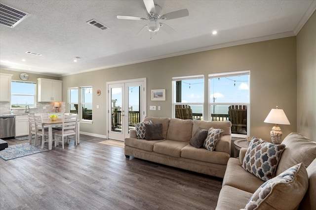 living room featuring wood-type flooring, ornamental molding, a water view, a textured ceiling, and french doors