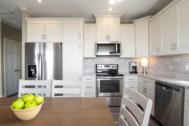 kitchen with appliances with stainless steel finishes, white cabinets, decorative backsplash, crown molding, and light stone countertops