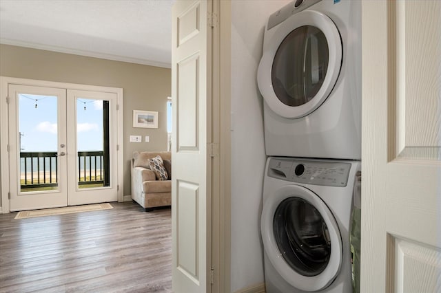 laundry room featuring stacked washing maching and dryer, crown molding, light hardwood / wood-style floors, and french doors