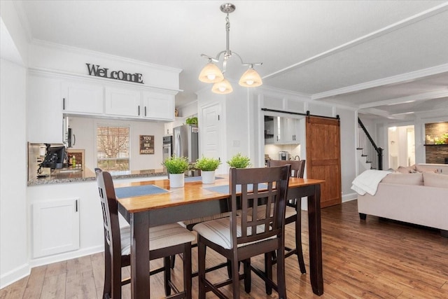 dining space featuring an inviting chandelier, ornamental molding, a barn door, and light wood-type flooring