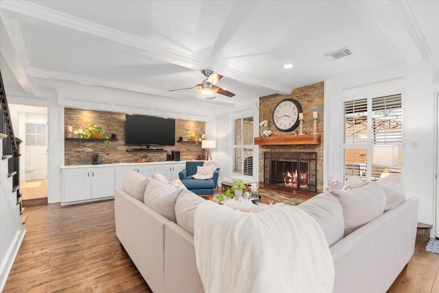 living room with crown molding, ceiling fan, beam ceiling, a fireplace, and light wood-type flooring