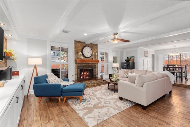 living room with beamed ceiling, crown molding, a stone fireplace, and light wood-type flooring