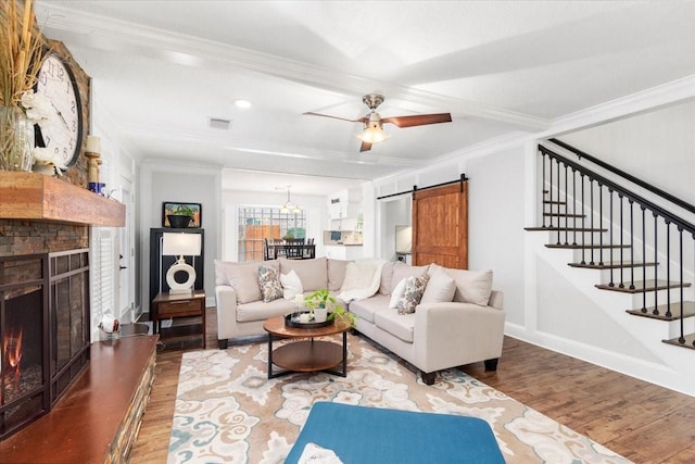 living room with ceiling fan, hardwood / wood-style floors, a fireplace, ornamental molding, and a barn door