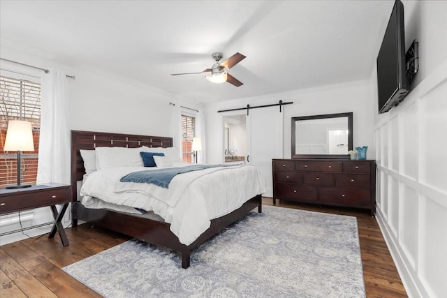 bedroom with crown molding, a barn door, dark hardwood / wood-style floors, and ceiling fan