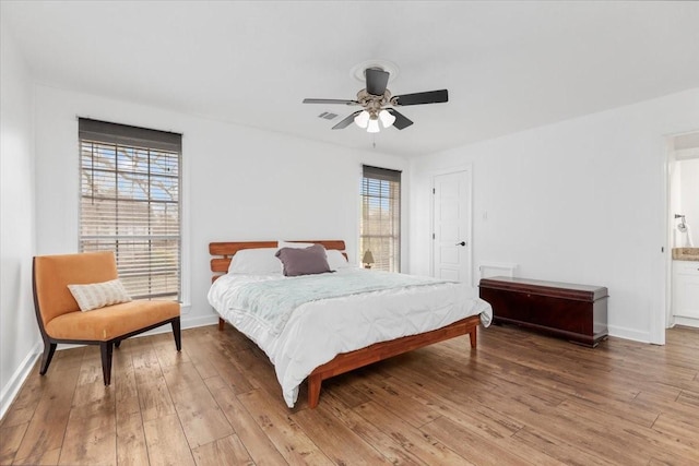 bedroom with multiple windows, wood-type flooring, ensuite bathroom, and ceiling fan