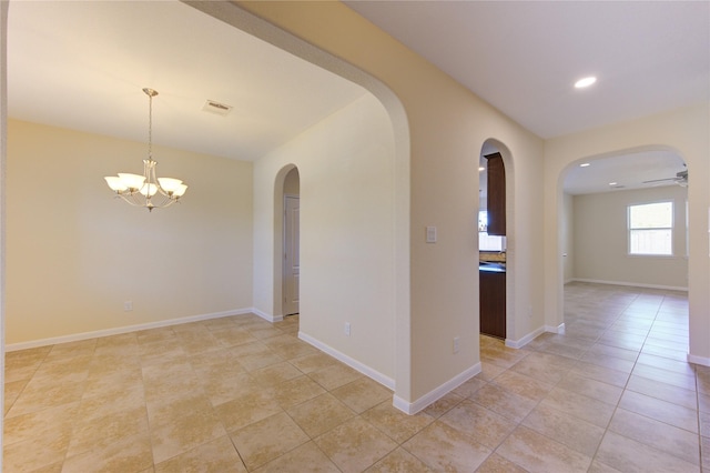 tiled spare room featuring ceiling fan with notable chandelier