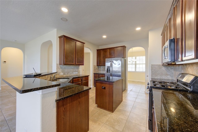 kitchen with sink, dark stone countertops, stainless steel appliances, a kitchen island, and decorative backsplash