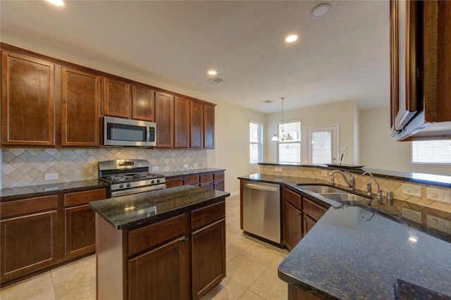 kitchen featuring sink, decorative light fixtures, a center island, dark stone countertops, and stainless steel appliances