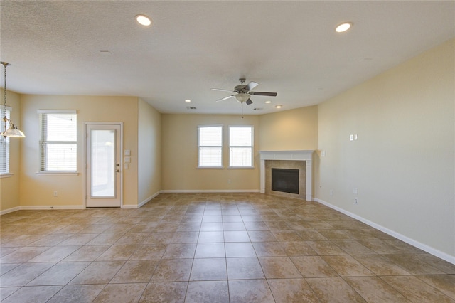 unfurnished living room featuring ceiling fan, a textured ceiling, a tile fireplace, and light tile patterned floors