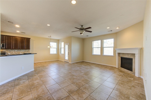 unfurnished living room featuring light tile patterned flooring, ceiling fan, plenty of natural light, and a tile fireplace