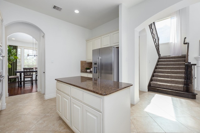 kitchen featuring a kitchen island, dark stone countertops, light tile patterned floors, and stainless steel fridge with ice dispenser