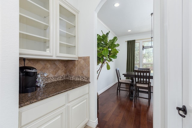 kitchen with dark wood-type flooring, backsplash, ornamental molding, white cabinets, and dark stone counters