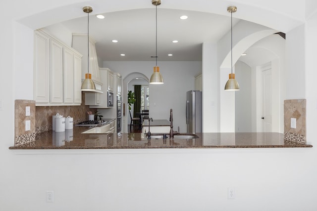 kitchen featuring sink, dark stone countertops, kitchen peninsula, and decorative light fixtures