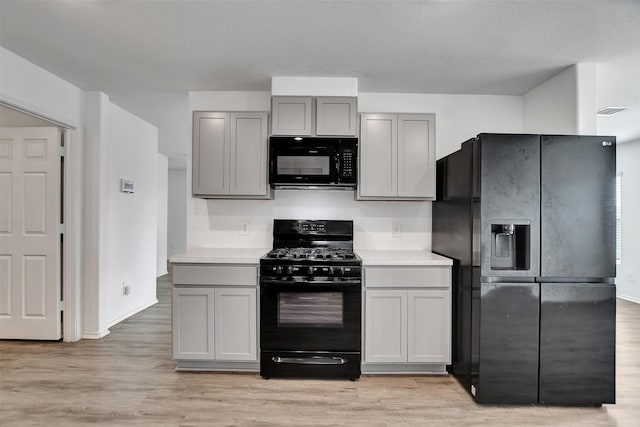 kitchen with gray cabinets, a textured ceiling, light hardwood / wood-style flooring, and black appliances