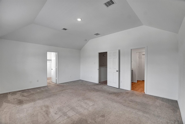 unfurnished bedroom featuring vaulted ceiling, a walk in closet, light carpet, and a closet