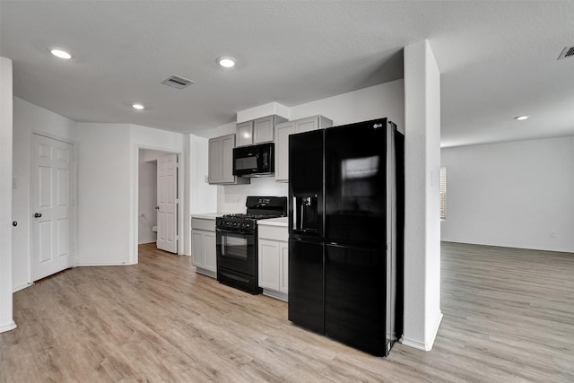 kitchen with black appliances, a textured ceiling, and light wood-type flooring