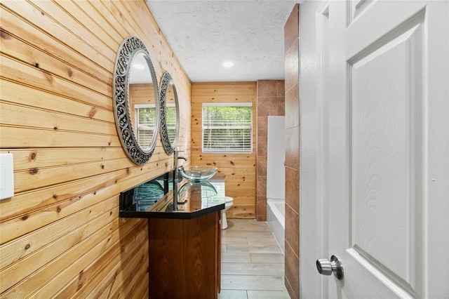 bathroom with vanity, wooden walls, toilet, and a textured ceiling